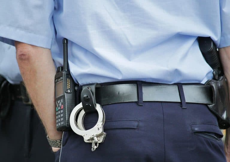 The backside of a white police officer wielding handcuffs and a walkie-talkie..