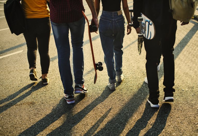 Four teens walking down a street into the sunset with longboards