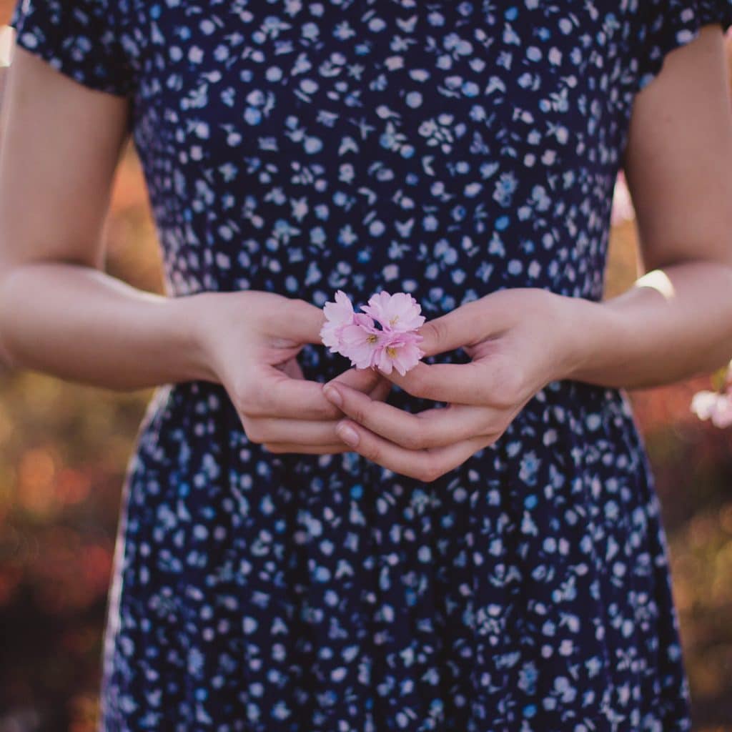 A woman holds a flower in front of her torso
