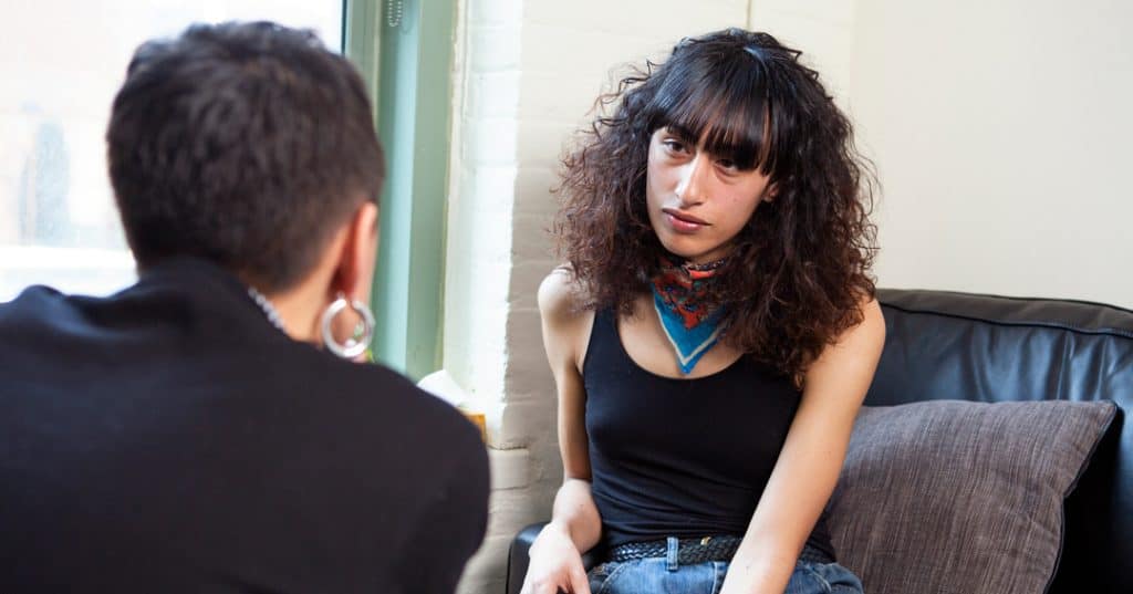 A transgender woman sitting on a couch and listening.