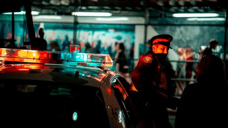 Police officer standing next to a cop car with its lights on as he talks to a women