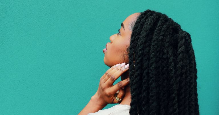 Black women looking off into the sky standing by a teal wall