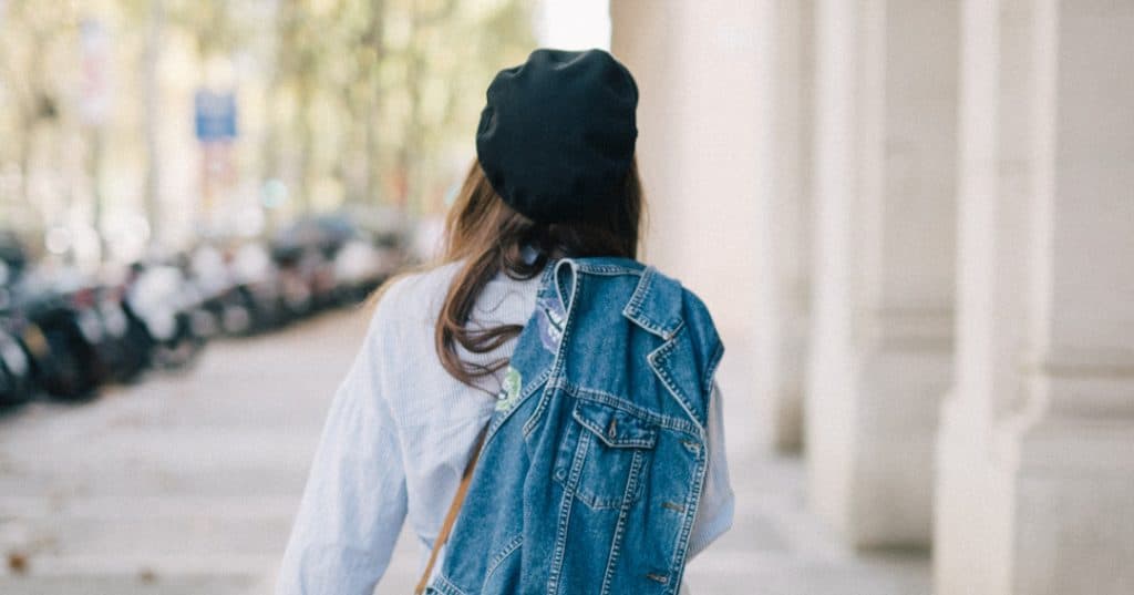 Women walking away from the camera down a sunny street with a denim jacket slung over her shoulder.