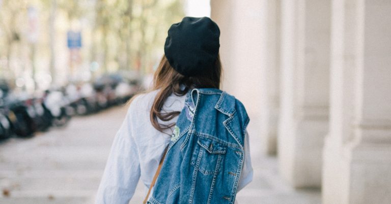 Women walking away from the camera down a sunny street with a denim jacket slung over her shoulder.