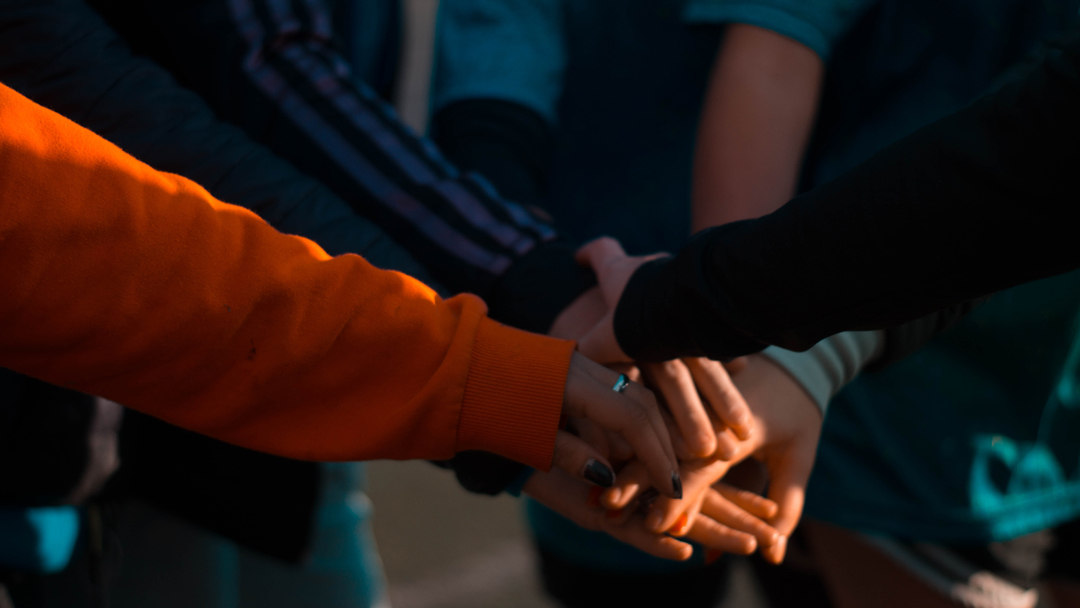 A close up image of a group of people standing in a circle with their hands extended into the middle