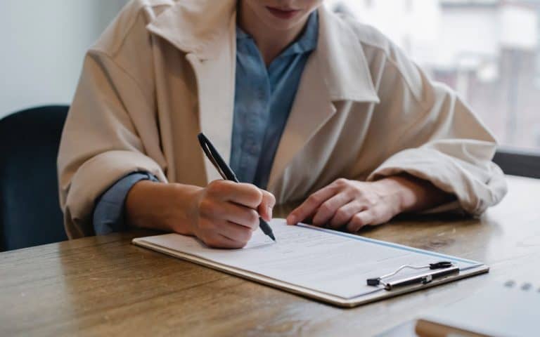 Women leaning over a desk, filling out paperwork with a pen