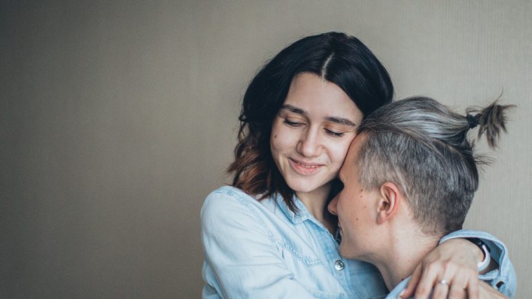 Two people embrace, with the person on the left closing their eyes.
