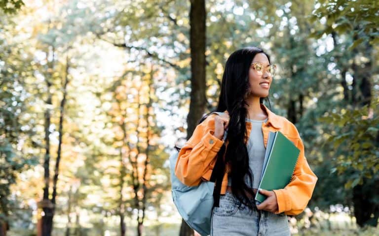 Women with long black hair walking on a tree lined campus path looking into the distance and smiling