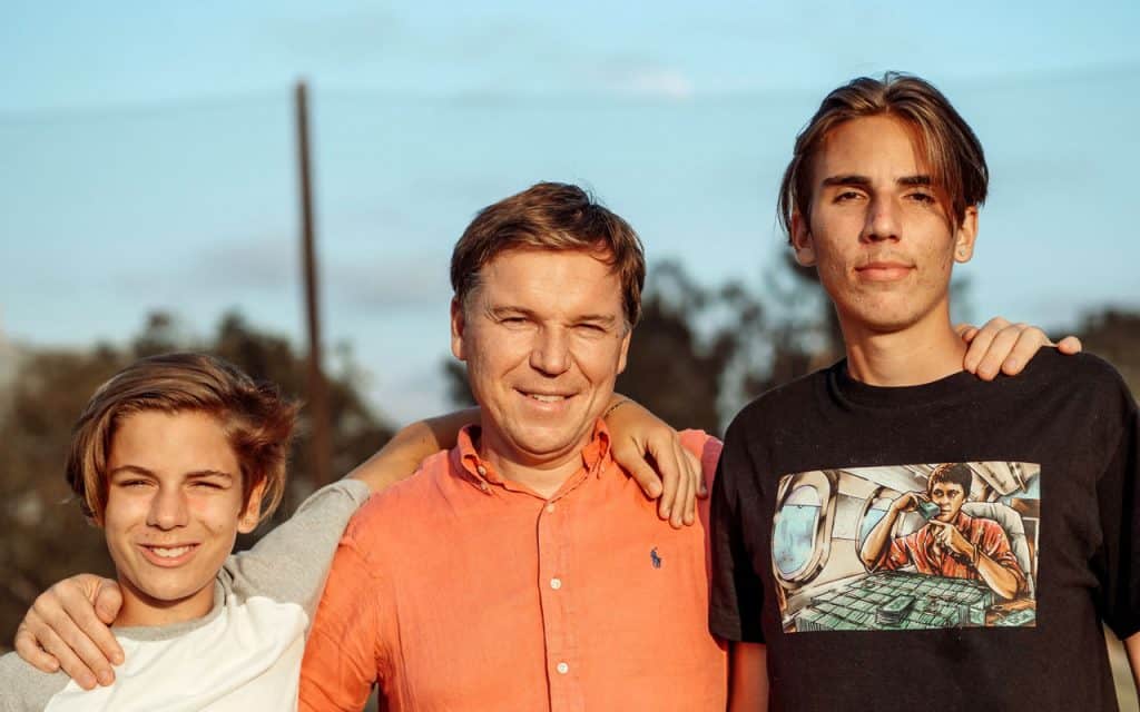 An older masculine-presenting person stands with their arm around two younger masc-presenting teens.