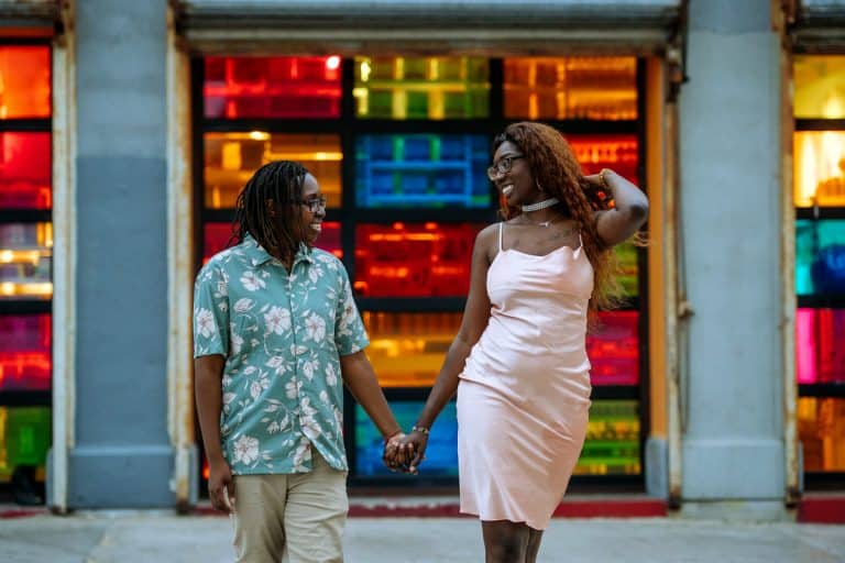 Two Black women holding hands and smiling in front of colorful stained glass