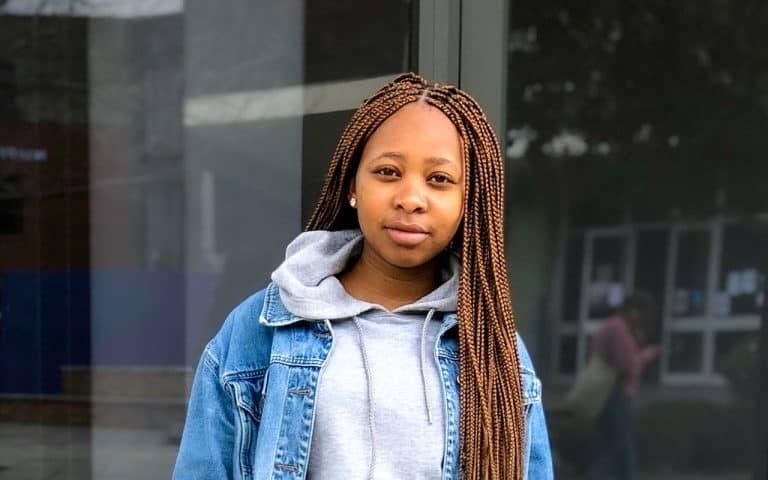 Black teen girl with a hopeful expression, wearing long braids, a grey hoodie, and a denim jacket, stares into the camera.