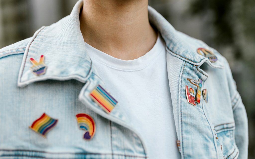 Close up image of a person wearing a denim jacket with multiple LGBTQ+ pride pins