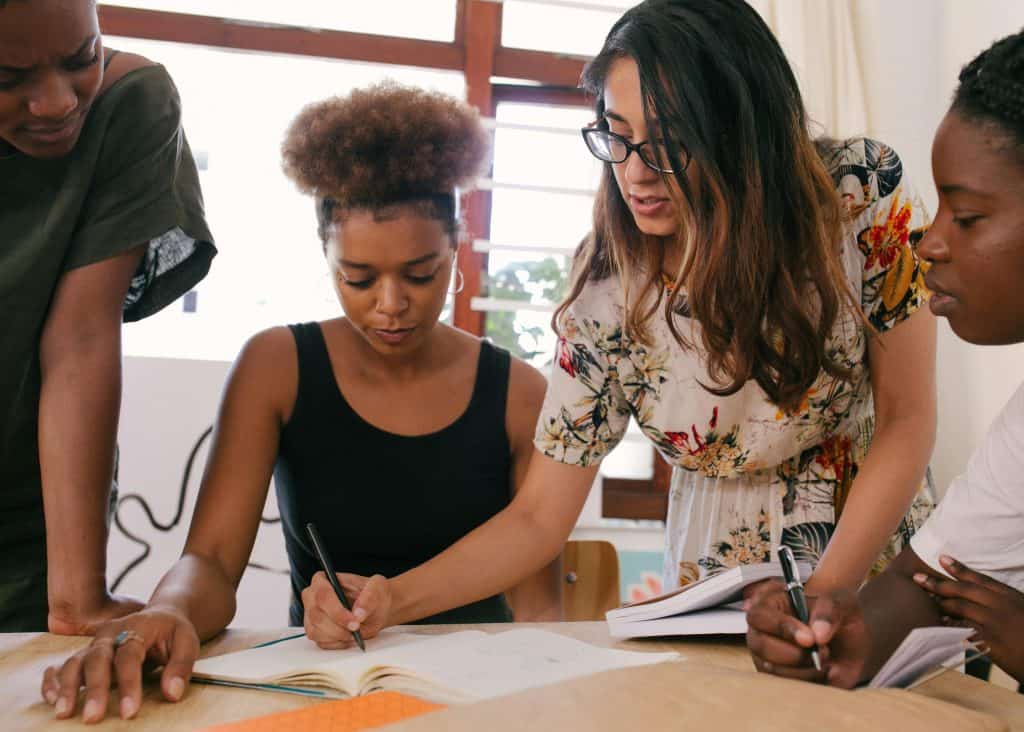Four friends are gathered around a notebook writing and talking to each other.