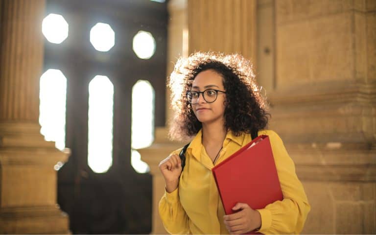 Student walks in a building holding a binder.