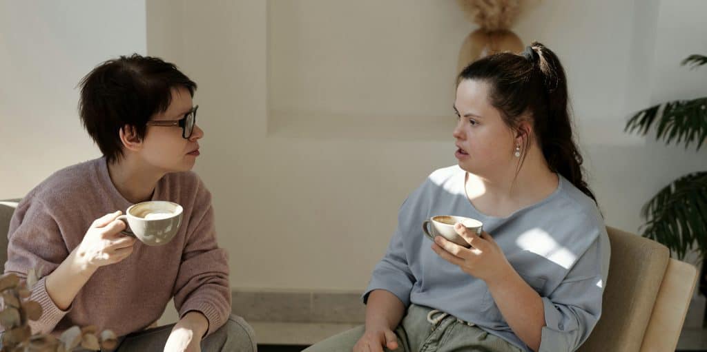 Two women in a sunny indoor space are sitting and talking.