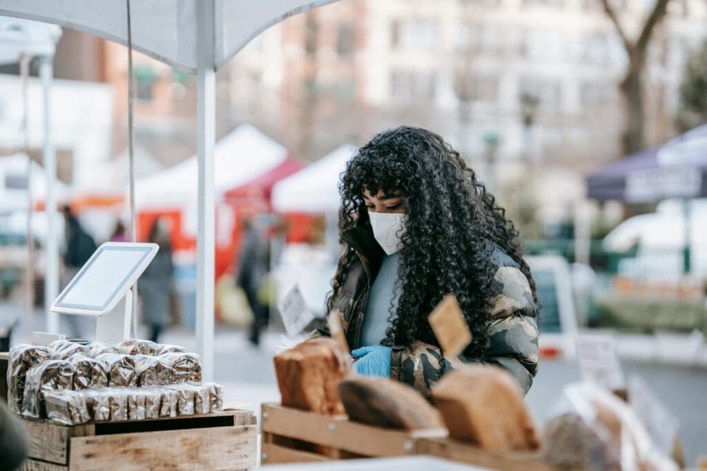 A women with long curly hair looks at various goods at a farmers market.