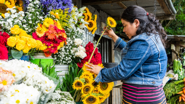 A women stands in front of a flower stand and pulls out a sunflower.