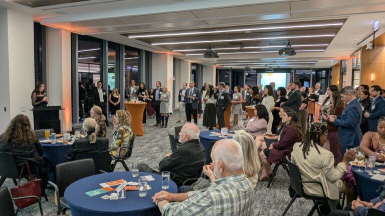 Photo shows Celebrating Allies attendees all gathered for the event, looking towards a person speaking into a microphone at the front of the room.