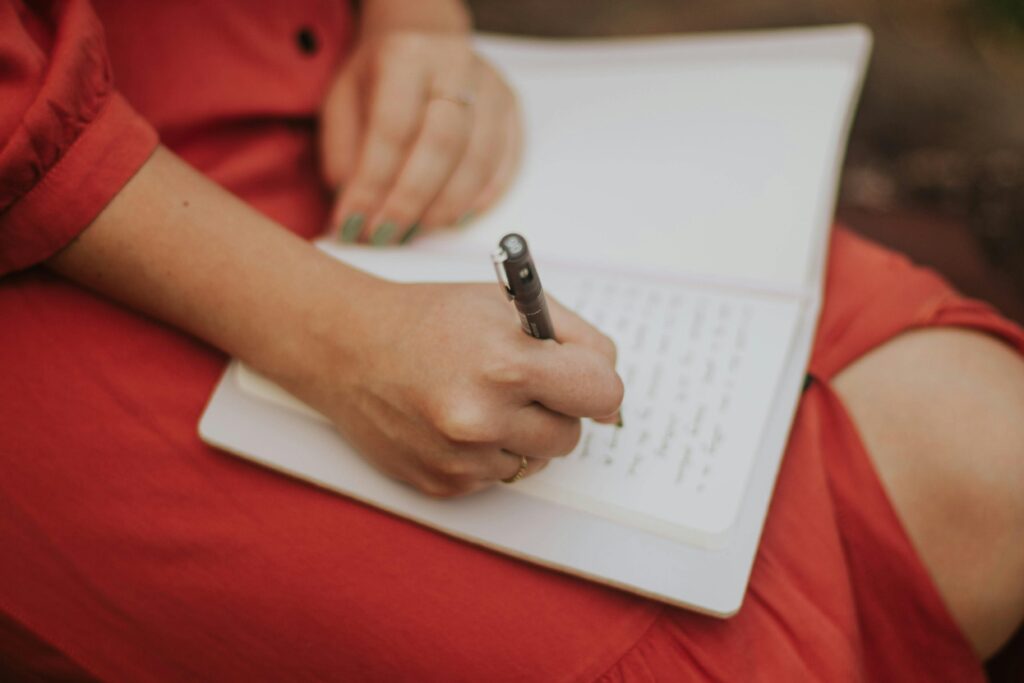 Photo of a women's hand writing in a notebook on her lap.
