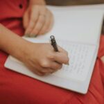 Photo of a women's hand writing in a notebook on her lap.