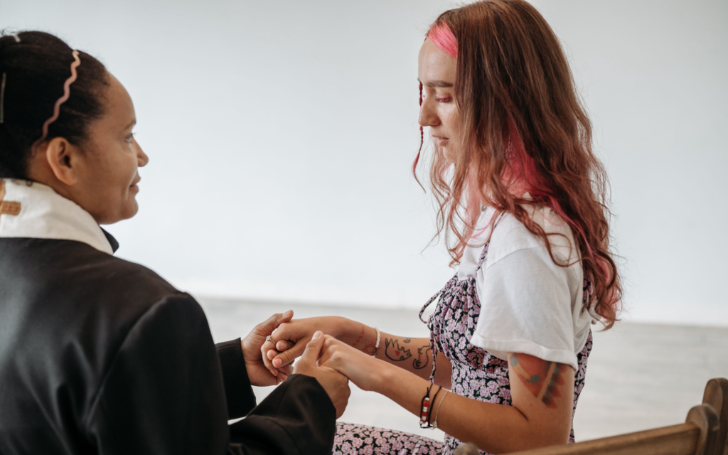 Two women face one another and hold hands, supporting one another.